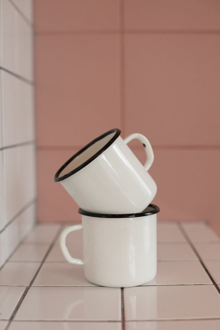 Close-up of two stacked enamel mugs on white tiled surface with pastel background.